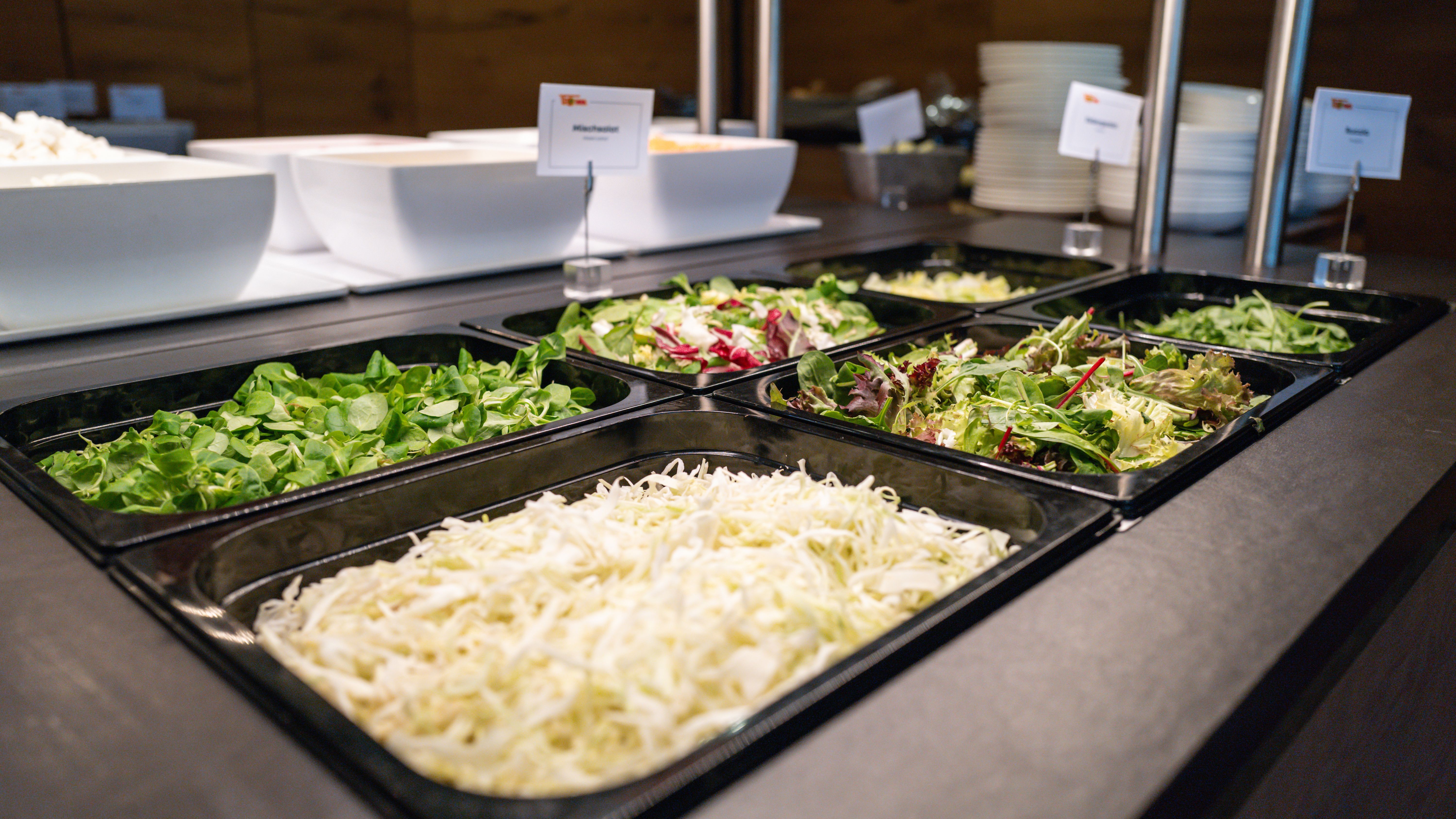 Ein Buffet mit verschiedenen Salatsorten in schwarzen Schalen, darunter Kopfsalat, Weißkraut und gemischte Blattsalate.